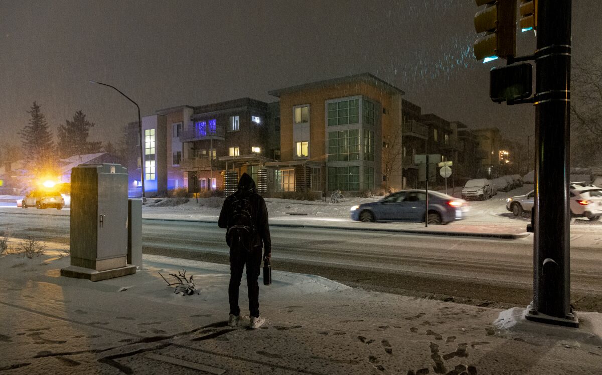 A person stands at a snow-covered intersection across from a modern apartment building