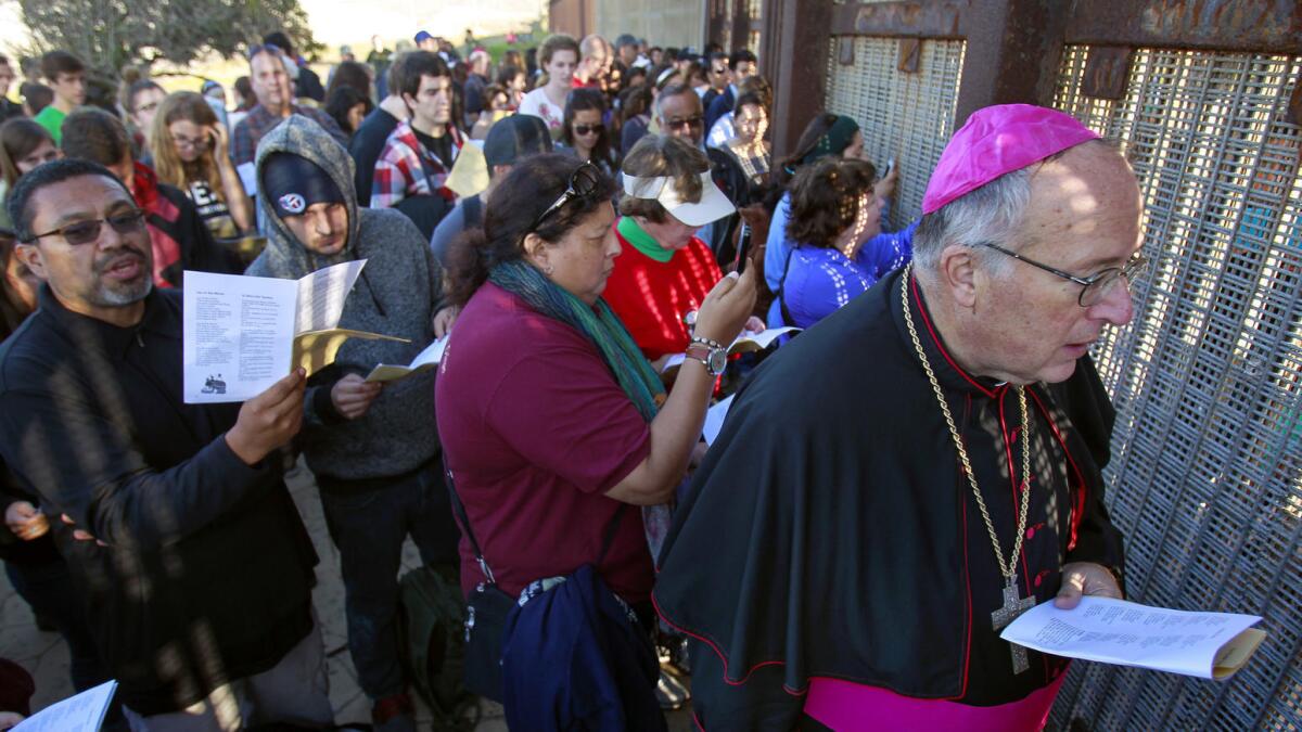 Bishop Robert McElroy and a crowd of people sing to those on the Tijuana side of the U.S.-Mexico border fence.