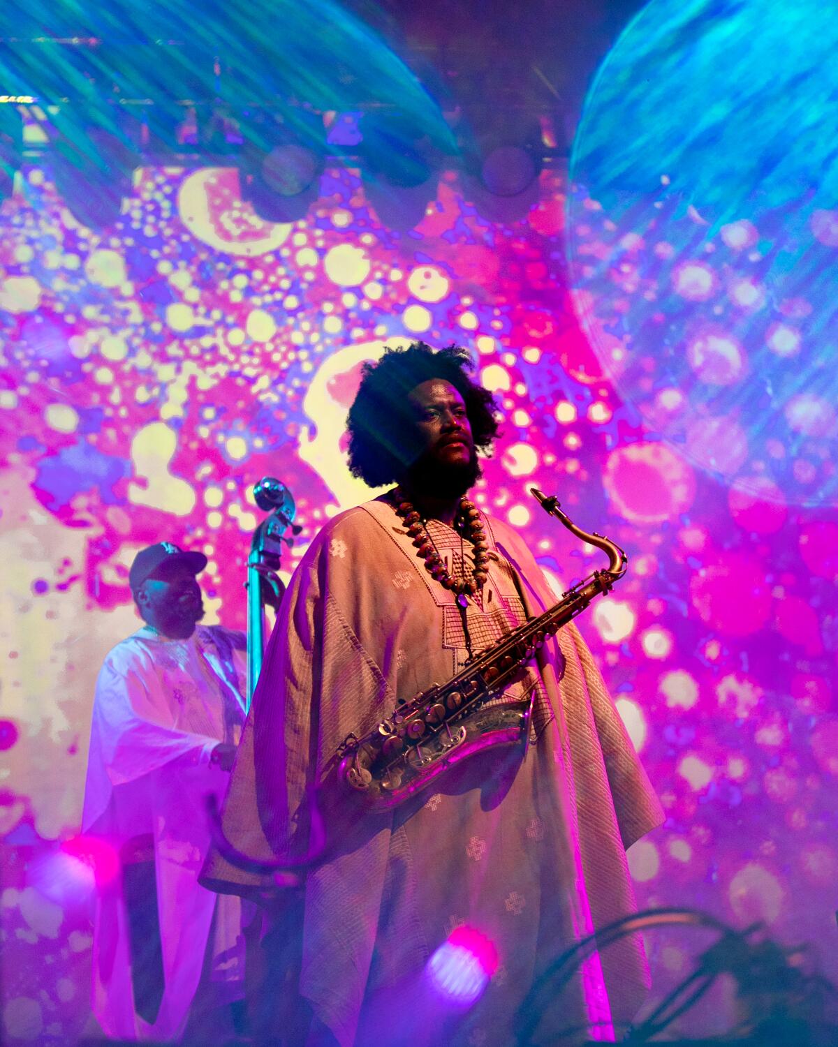 A saxophone player in a dashiki stands in front of a psychedelic backdrop