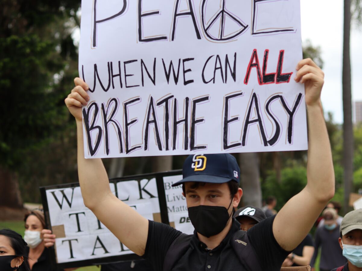 A person holds a sign that says "Peace when we can all breathe easier."