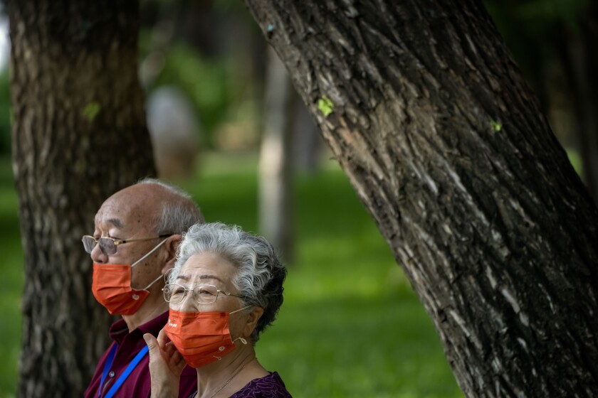 People wearing face masks sit on a bench at a public park in Beijing, Friday, July 8, 2022. The Chinese capital Beijing appears to have backed off a plan to launch a vaccine mandate for entry into certain public spaces after pushback from residents. (AP Photo/Mark Schiefelbein)