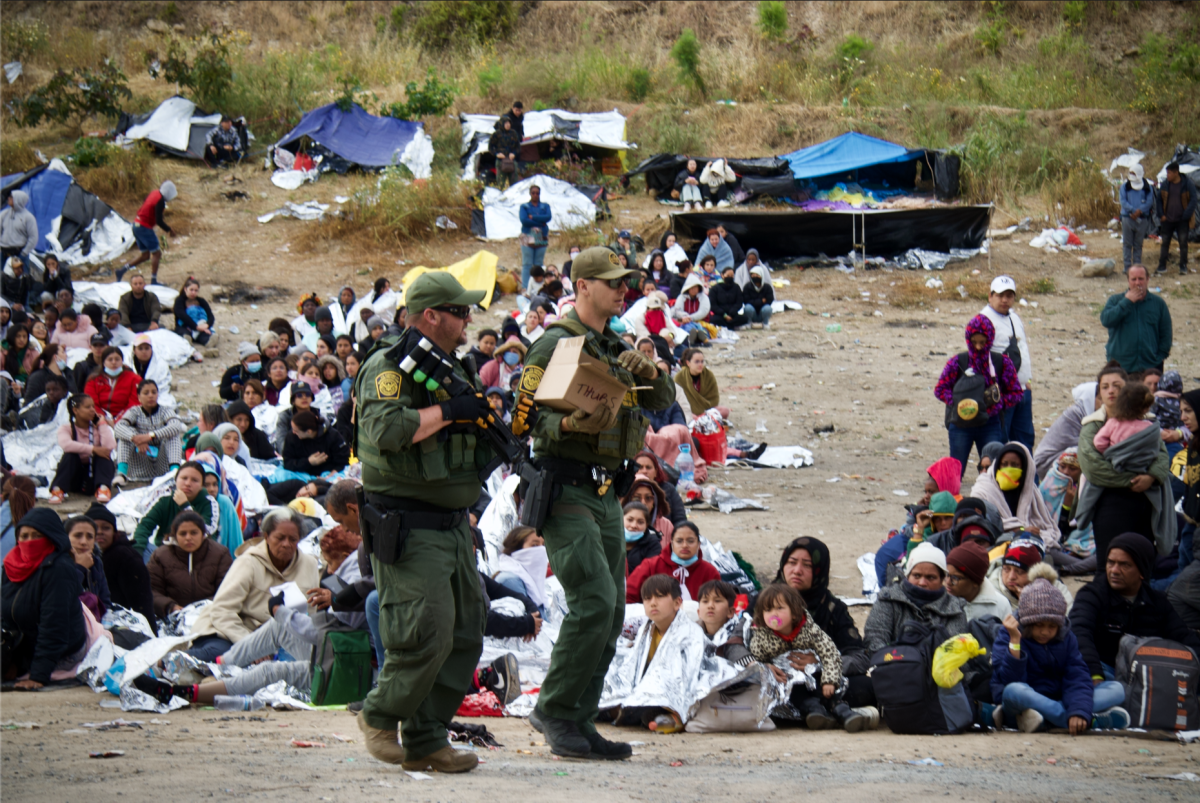 Migrantes estacionados entre los dos muros fronterizos en mayo.