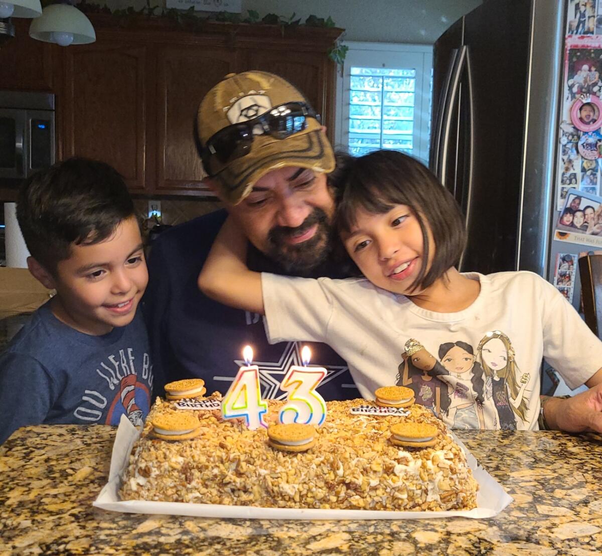 A man with two children in front of a cake with "43" in candles
