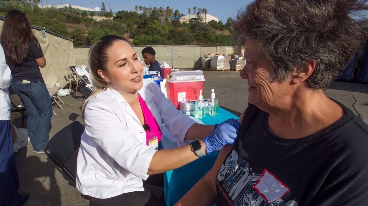 San Diego County Public health nurse Summer Leal puts a Bandaid Terrie Woolever's upper arm after giving her a hepatitis shot at the City of San Diego's new tent city at 20th and B streets Monday.