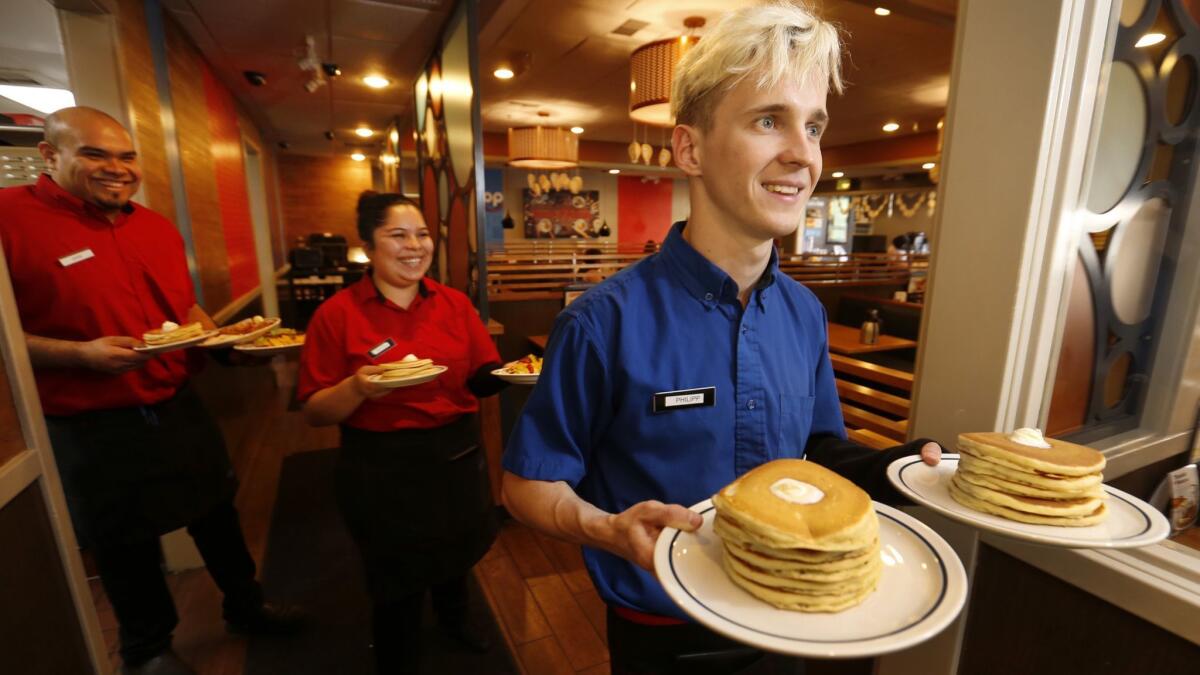 Servers carry plates of pancakes at an IHOP restaurant. The chain has to agreed to scrap its policy against worker poaching among franchises.