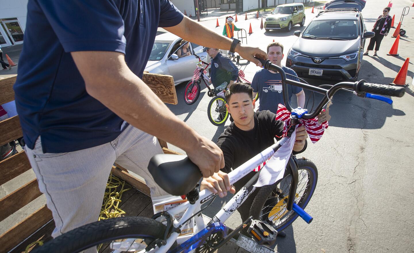 Proponent's Bobby Echeveirra hands off a bike to his colleague Christian Son at the collection center for the Share Our Selves (SOS) annual Adopt A Family Program at the OC Fair & Event Center on Tuesday. The program, which connects struggling Orange County families with community members who provide gifts and food for the holidays, is in its 49th year.