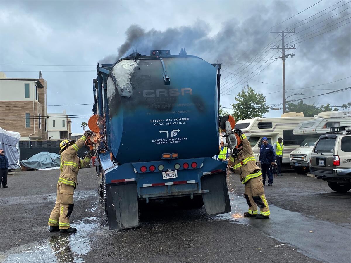 Costa Mesa fire crews work to gain access to the compartment of a trash truck that caught fire Monday on Placentia Avenue.