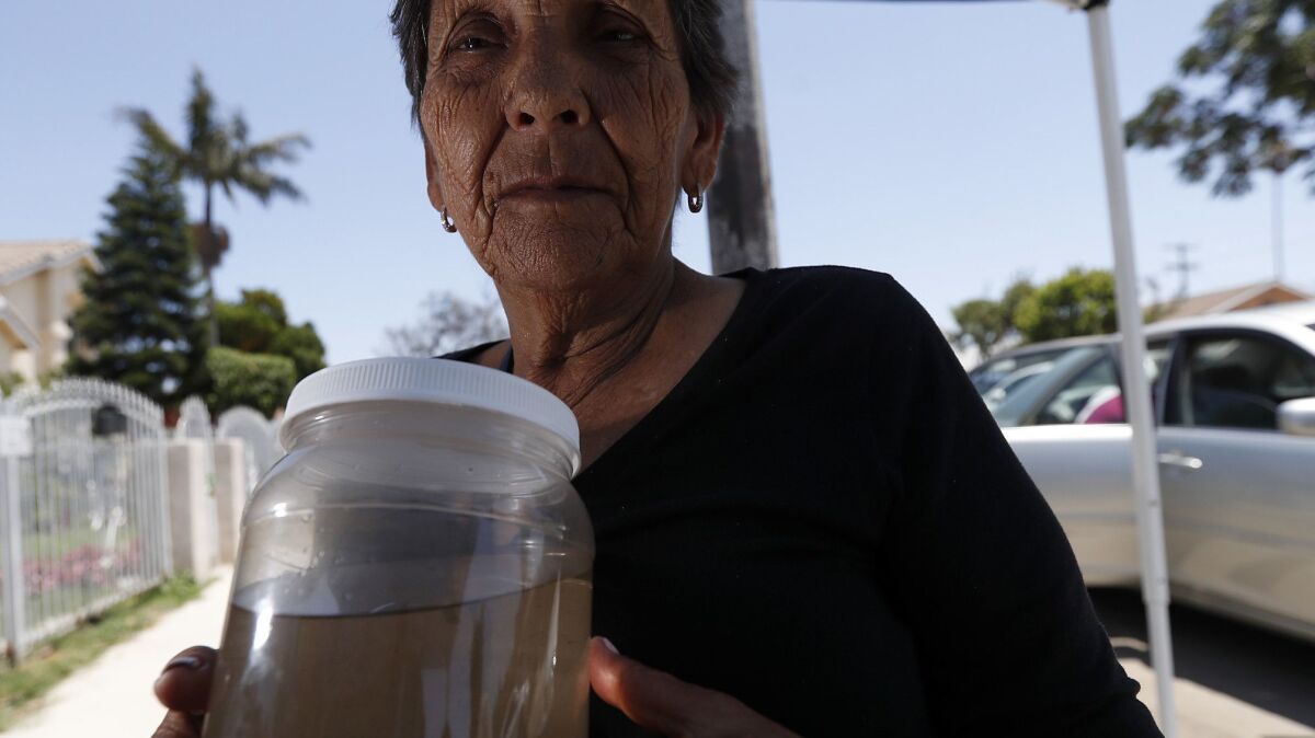 Compton resident Felicita Hernandez, 81, holds a container of discolored water from her faucet.