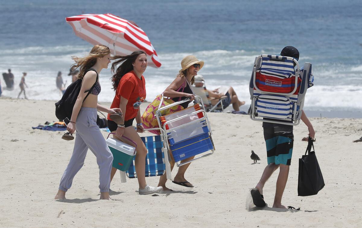 Beachgoers walk across the sand looking for a spot to post their chairs on a warm afternoon in Laguna Beach on Tuesday.