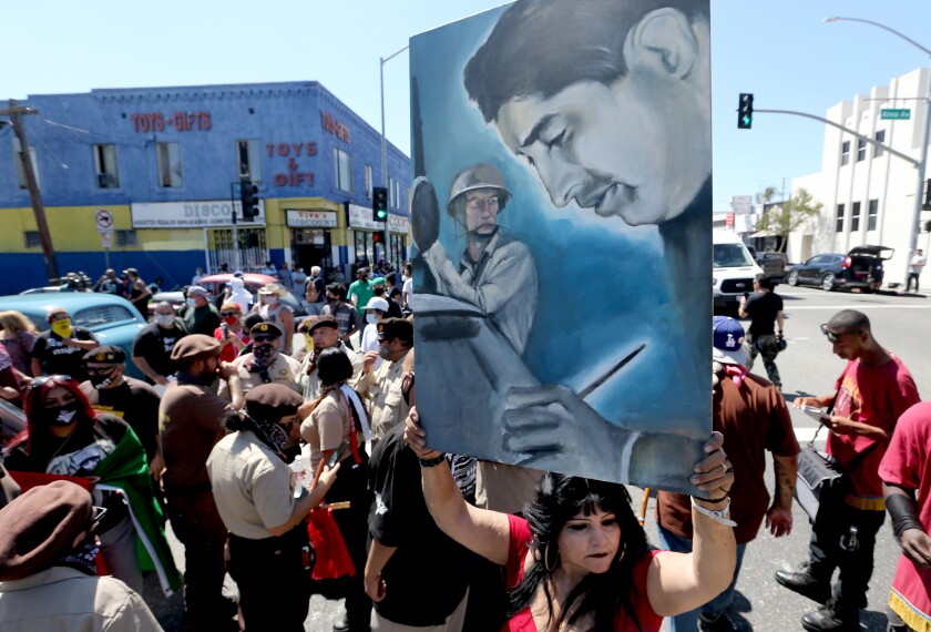 A protester raises a painting of slain journalist Ruben Salazar amid a crowd at the Chicano Moratorium anniversary march