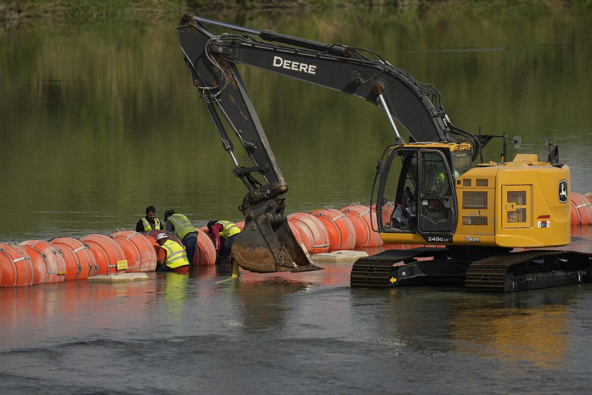 Workers use heavy machinery to adjust a floating barrier.