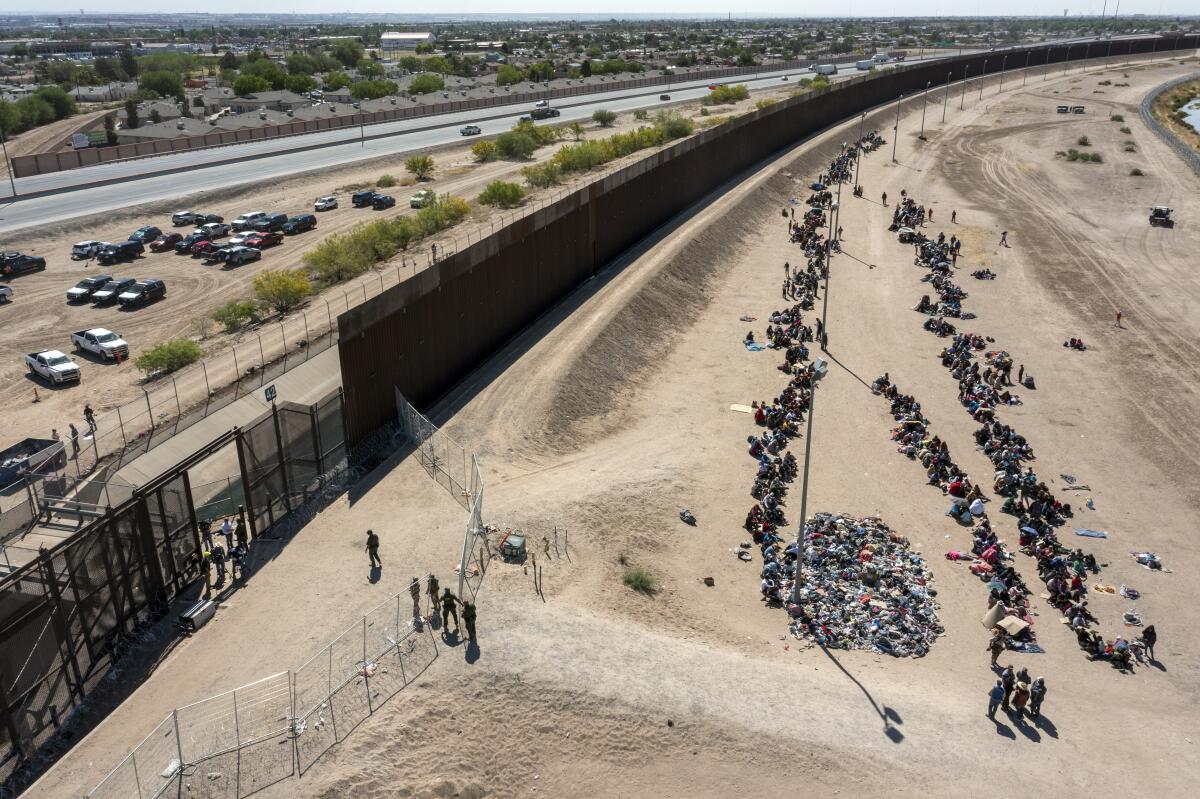 ARCHIVO - Migrantes forman filas frente a la valla en la frontera de Estados Unidos con México.