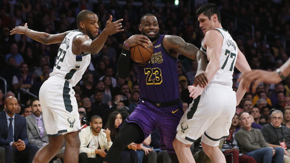 Lakers' LeBron James (23) is guarded by Milwaukee Bucks' Khris Middleton (22) and Ersan Ilyasova (77) in the second half.