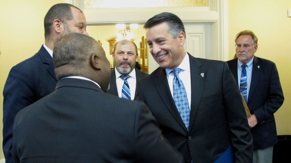 Nevada Republican Gov. Brian Sandoval greets Democratic Assembly Speaker Jason Frierson on his way into the Old Assembly Chambers for a budget bill-signing ceremony Monday at the state Capitol in Carson City, Nev.