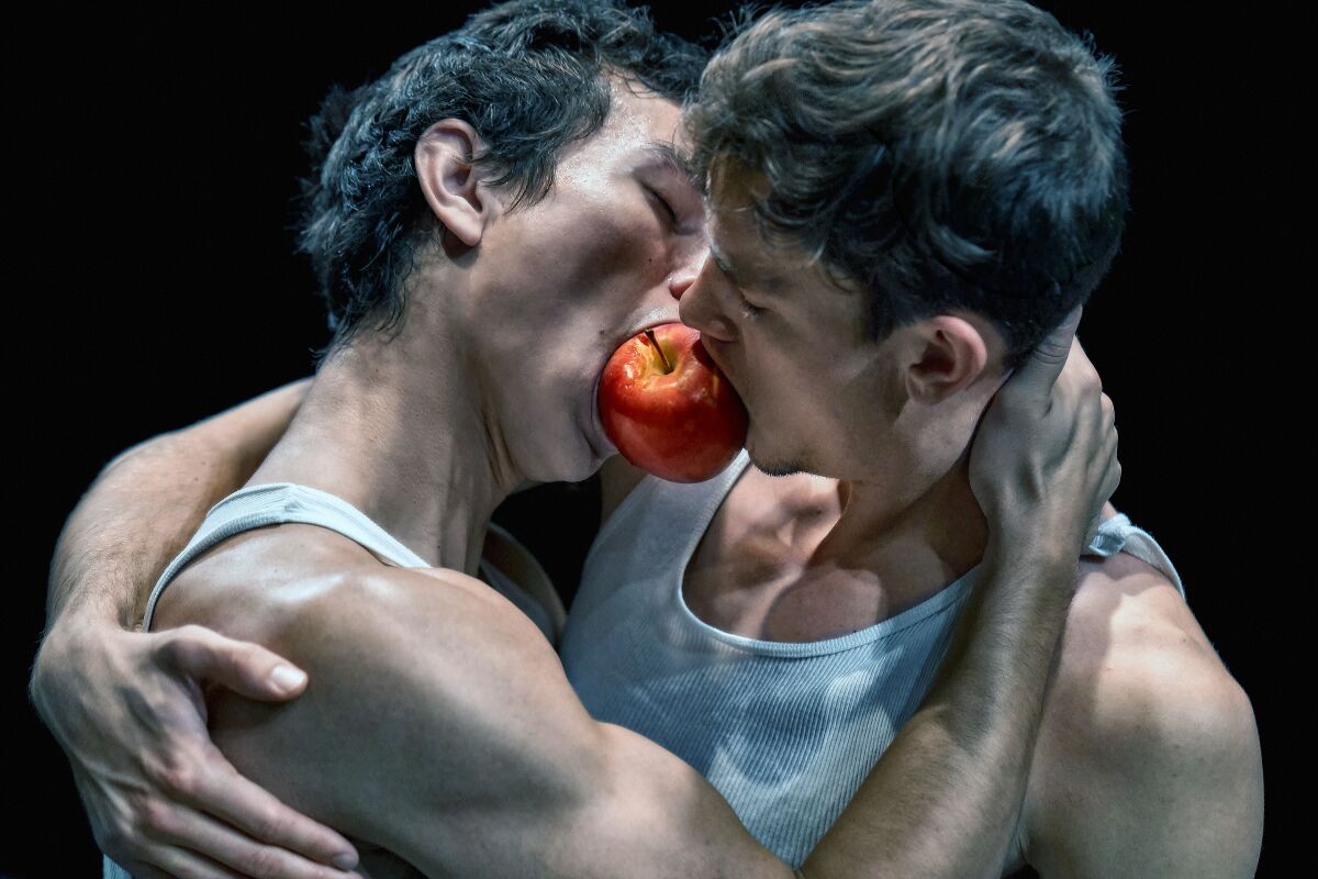 Two men dance the "apple duet," in an embrace and both biting into the same apple.
