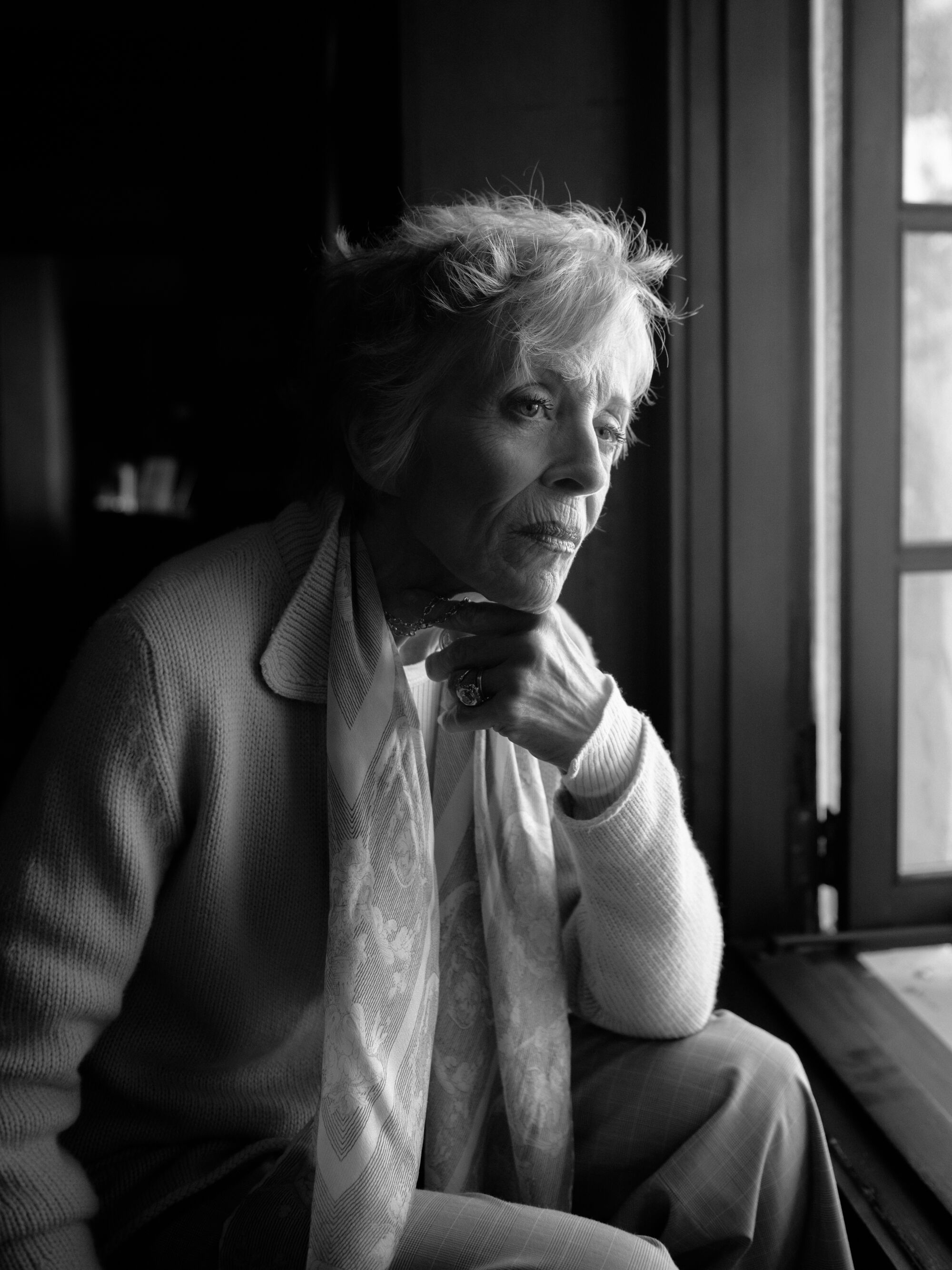 A black-and-white portrait of a seated woman looking out a window.