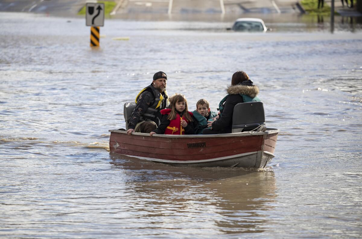 A woman and children who were stranded by high water due to flooding are rescued by a volunteer operating a boat in Abbotsford, British Columbia on Tuesday, Nov. 16, 2021. Officials in a small city near the Canada border are calling the damage devastating after a storm that dumped rain for days caused flooding and mudslides. City officials in Sumas, Washington said Tuesday that hundreds of people had been evacuated and estimated that 75% of homes had water damage. Just over the border, residents in about 1,100 rural homes in Abbotsford were told to evacuate as waterways started to rise quickly. (Darryl Dyck/The Canadian Press via AP)