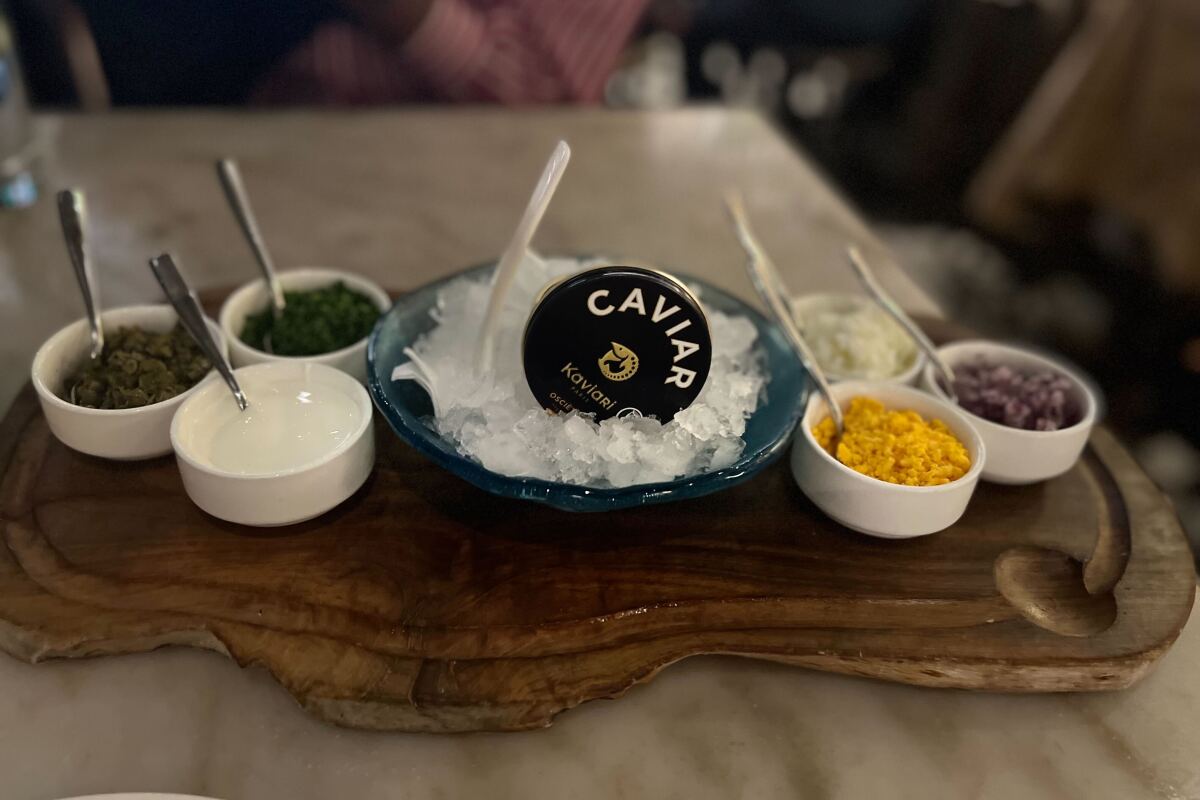 Small white ceramic dishes of caviar on a wooden platter