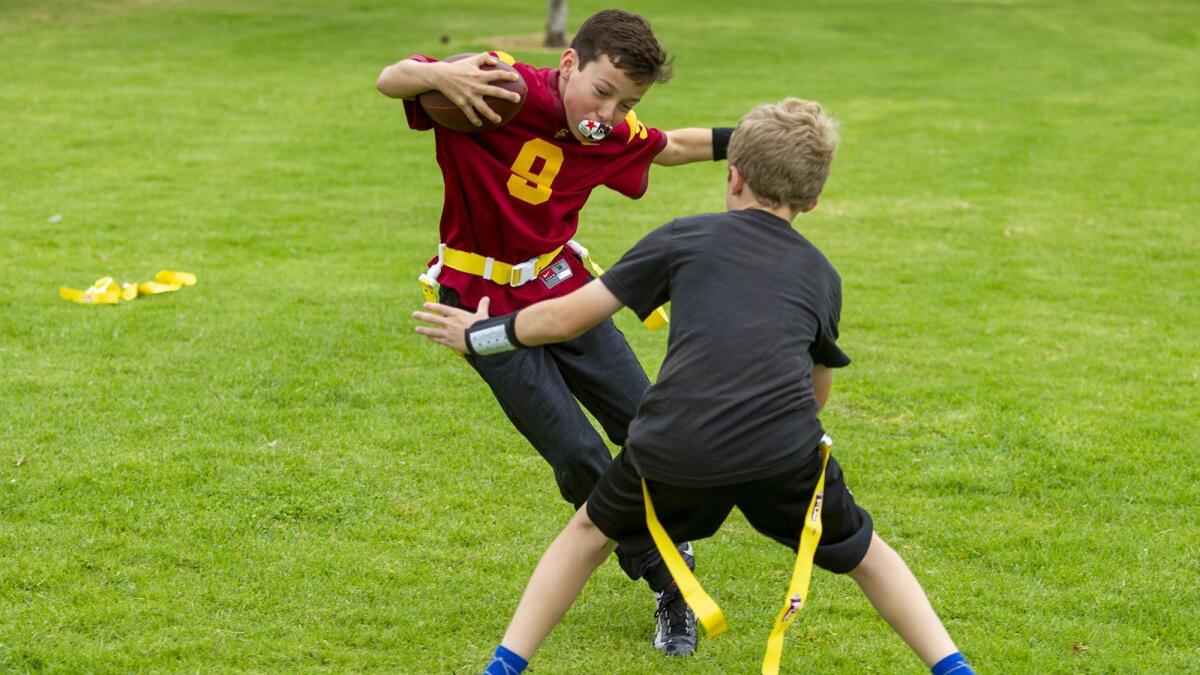 Bengals quarterback Jack Melenick, 11, left, tries to avoid teammate Ryan Pearson, also 11, during a practice with their flag football team at Costa Mesa’s Pinkley Park.