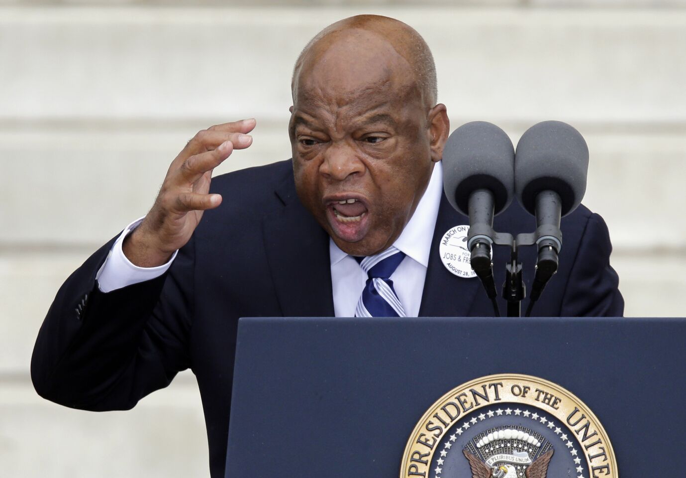 Rep. John Lewis gestures emphatically while speaking at a lectern during a commemoration of the March on Washington