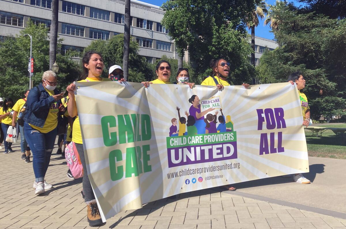 People wearing yellow T-shirts hold a banner reading "Child  care for all."