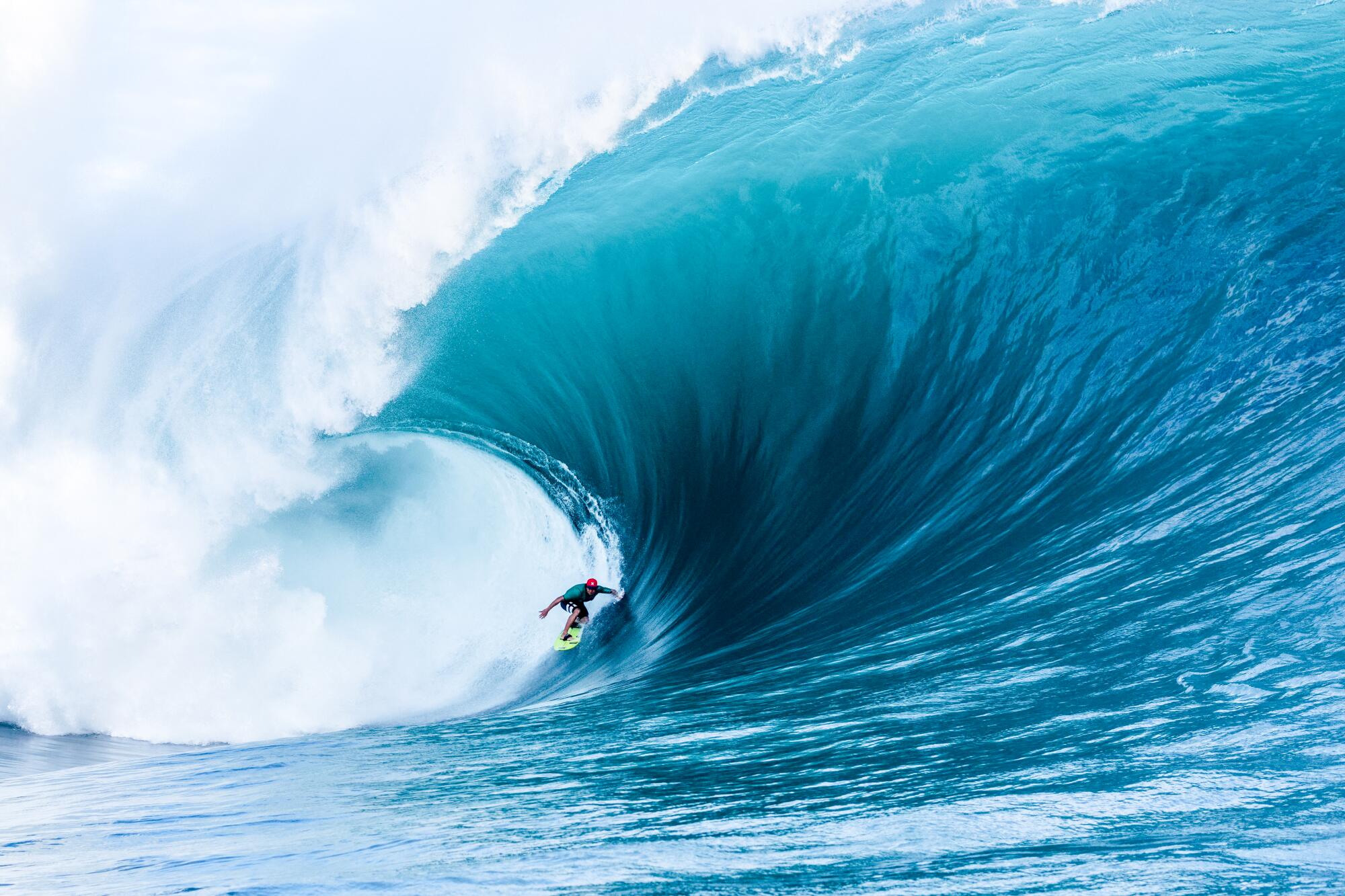 A lone surfer rides a massive, curling blue wave off the coast of Tahiti.
