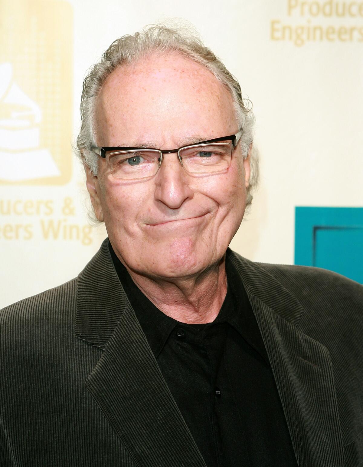 A man with gray hair, glasses and a wry smile, wearing black