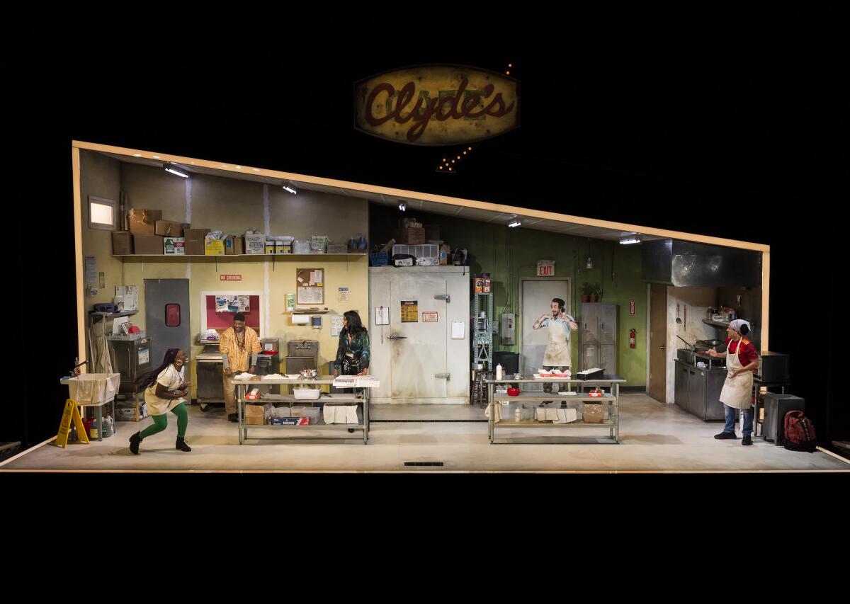 A wide shot of the "Clyde's" set shows a dingy commercial kitchen with employees spread under a canted ceiling.