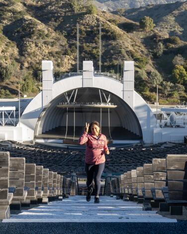 A runner flashes a peace sign as she runs up stairs at the Hollywood Bowl, its shell visible behind her.