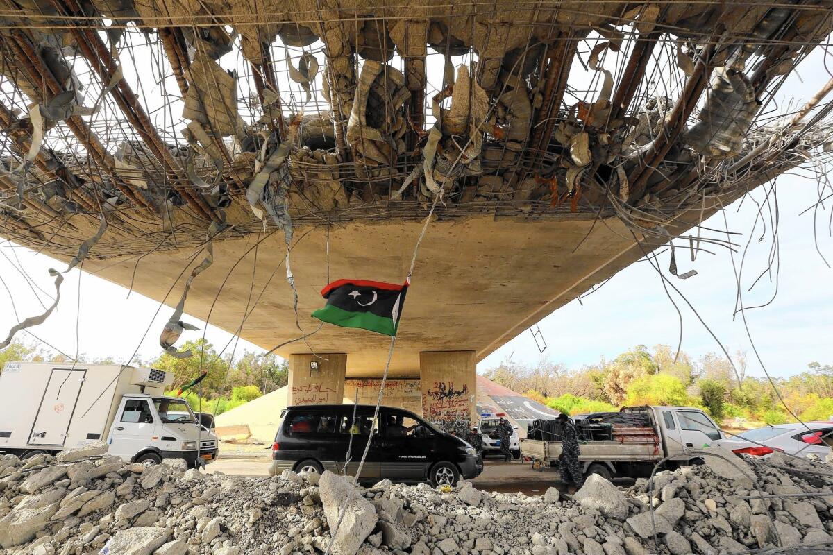 A Libyan flag flutters as cars wait at a police checkpoint near Tripoli, the capital. Neighborhoods in Tripoli and Benghazi have been smashed by battlefield-grade weapons. Most diplomats, aid groups and foreign enterprises have fled.