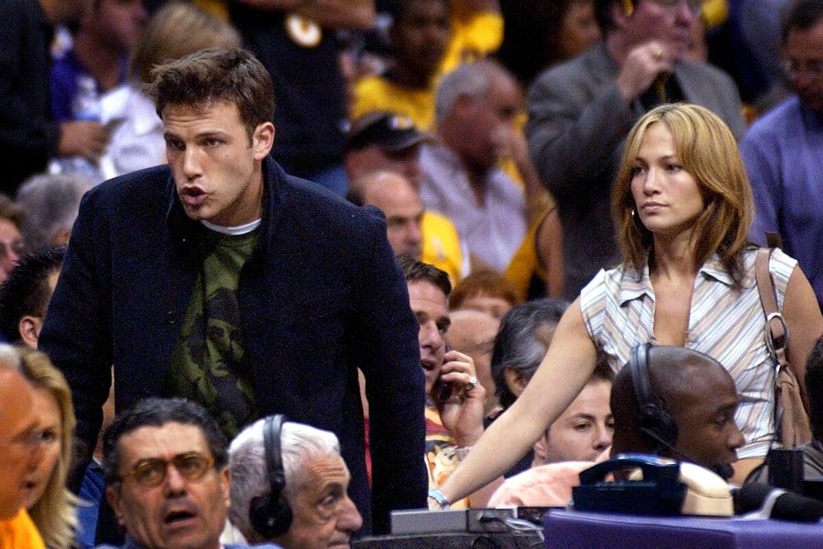 Ben Affleck and Jennifer Lopez standing and holding hands in a crowd of spectators