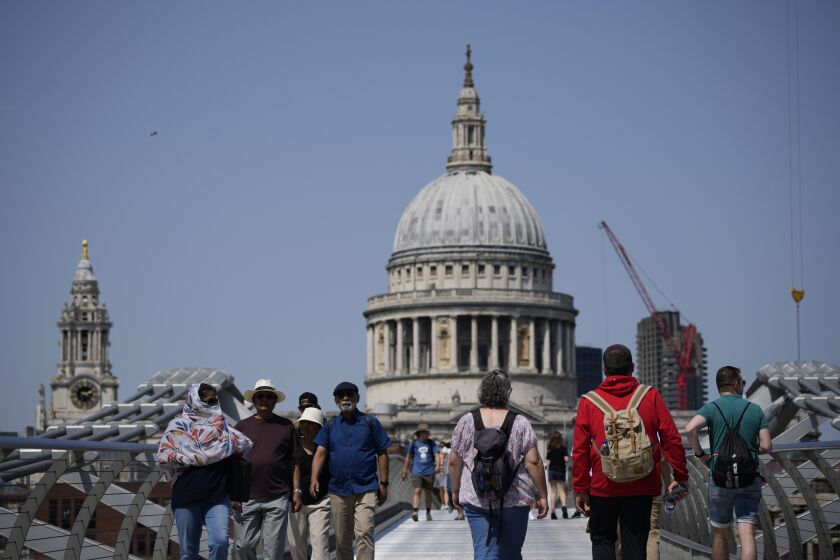 Some people cover their heads from the sun as they walk over the Millennium Bridge going over the River Thames, backdropped by the dome of St Paul's Cathedral, during hot weather in London, Monday, July 18, 2022. Britain's first-ever extreme heat warning is in effect for large parts of England as hot, dry weather that has scorched mainland Europe for the past week moves north, disrupting travel, health care and schools. (AP Photo/Matt Dunham)