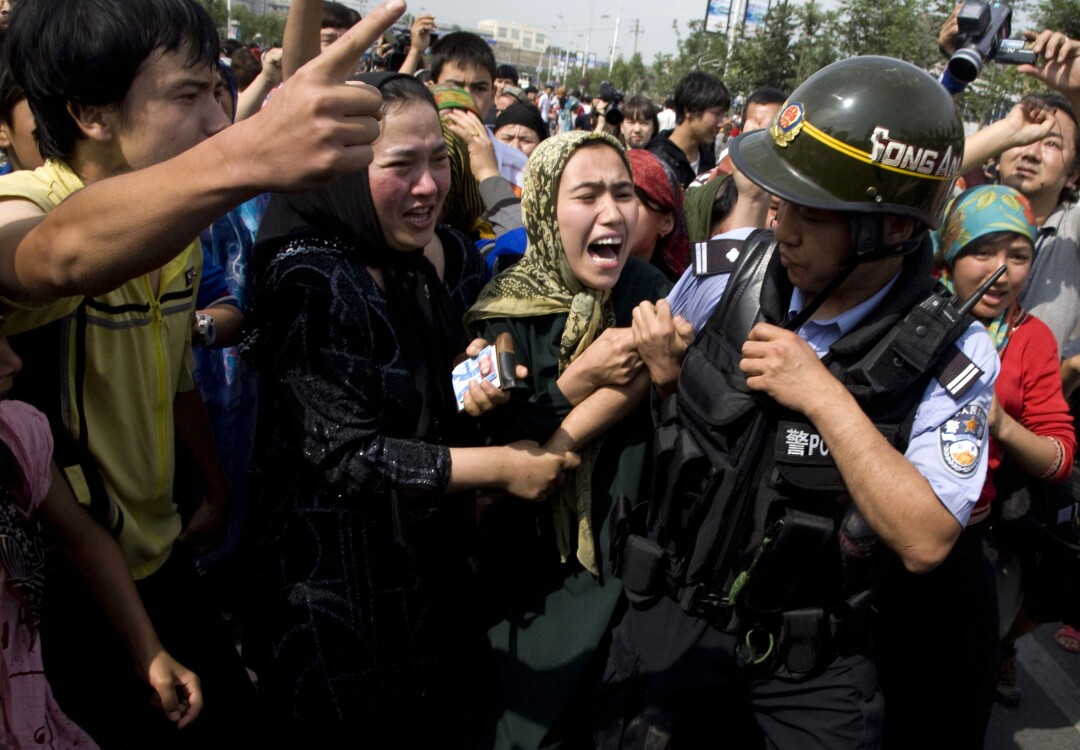 Uighur women grab a police officer as they protest in Urumqi, Xinjiang. 