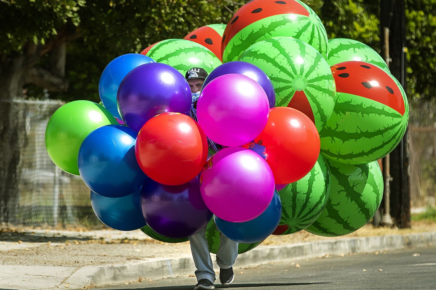Carlos Gutierrez creates his own shade while walking with inflatable balls for sale in Pacoima.