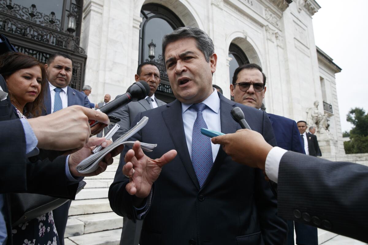 Honduran President Juan Orlando Hernandez speaks outside a building surrounded by microphones