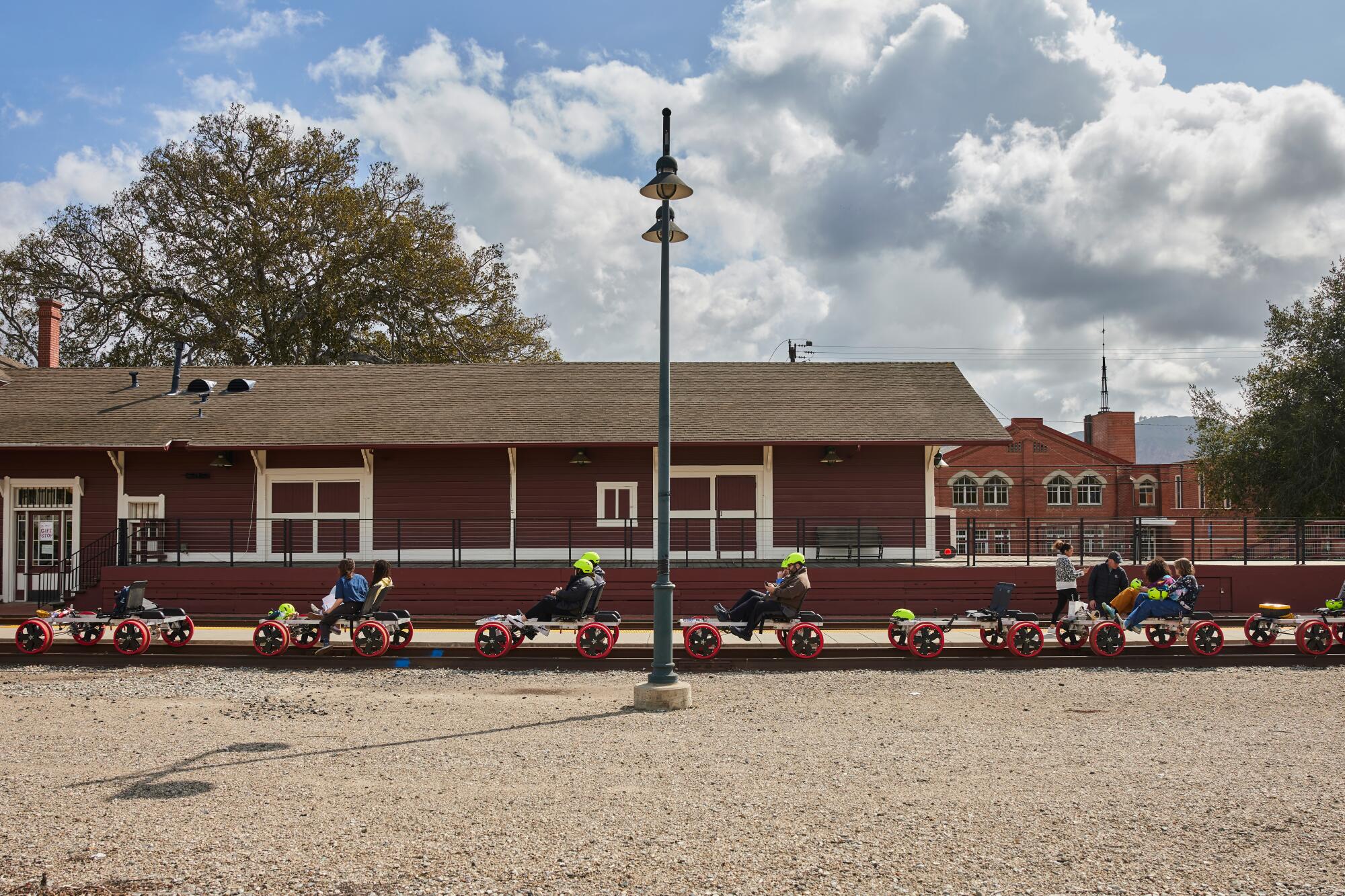 A scene-setting photo of a red building, with a set of train tracks in front of it holding seven railbikes, some with riders.