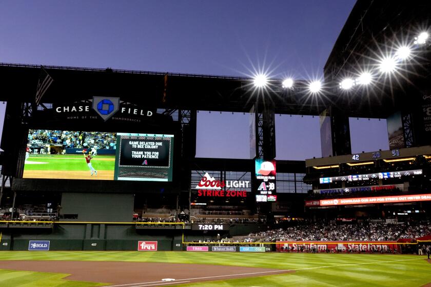 The scoreboard tells of a swarm of bees gathered on the net behind home plate delaying the start of a baseball game between the Los Angeles Dodgers and the Arizona Diamondbacks, Tuesday, April 30, 2024, in Phoenix. (AP Photo/Matt York)