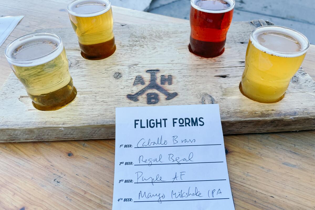 A flight of four taster beers in a wooden paddle on an outdoor patio, with a paper that says "Flight Forms"