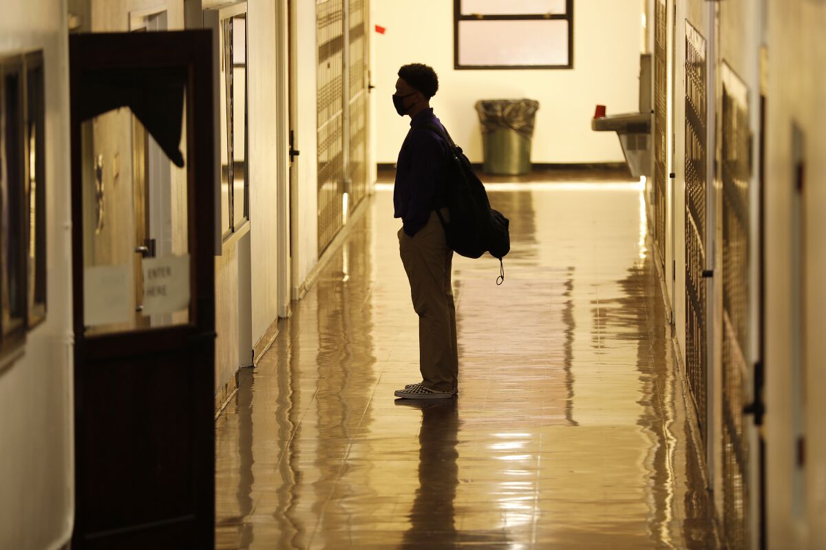 A masked student stands alone in a school hallway. 