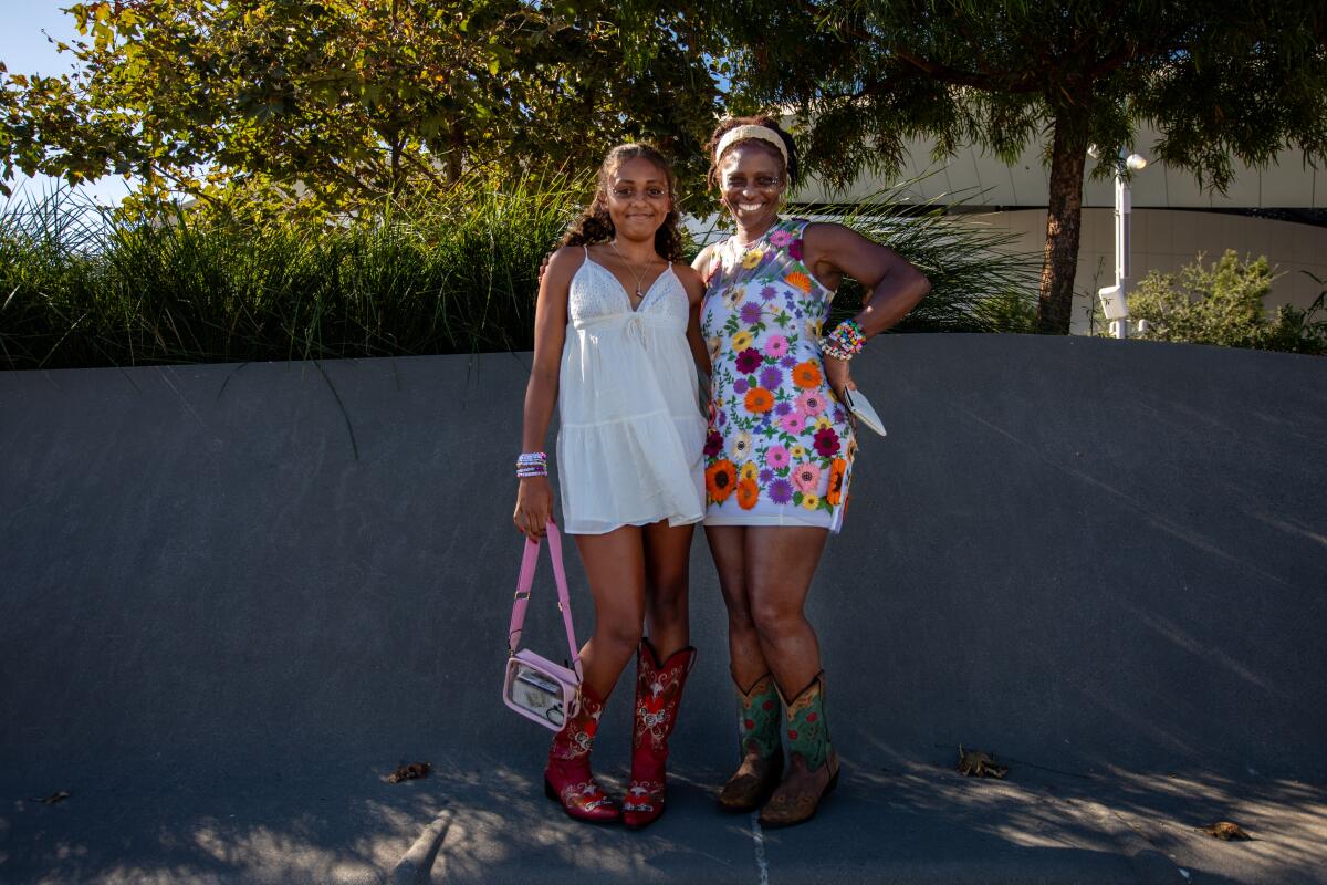 A young woman in a short white dress and boots poses with her mom, who wears a short floral dress and boots