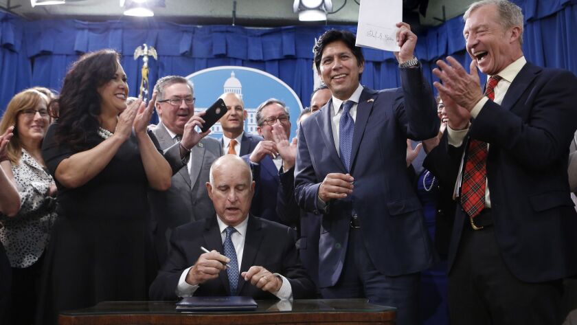 State Sen. Kevin de León (D-Los Angeles) holds up his environmental measure Senate Bill 100 after it was signed into law by Gov. Jerry Brown on Monday in Sacramento.