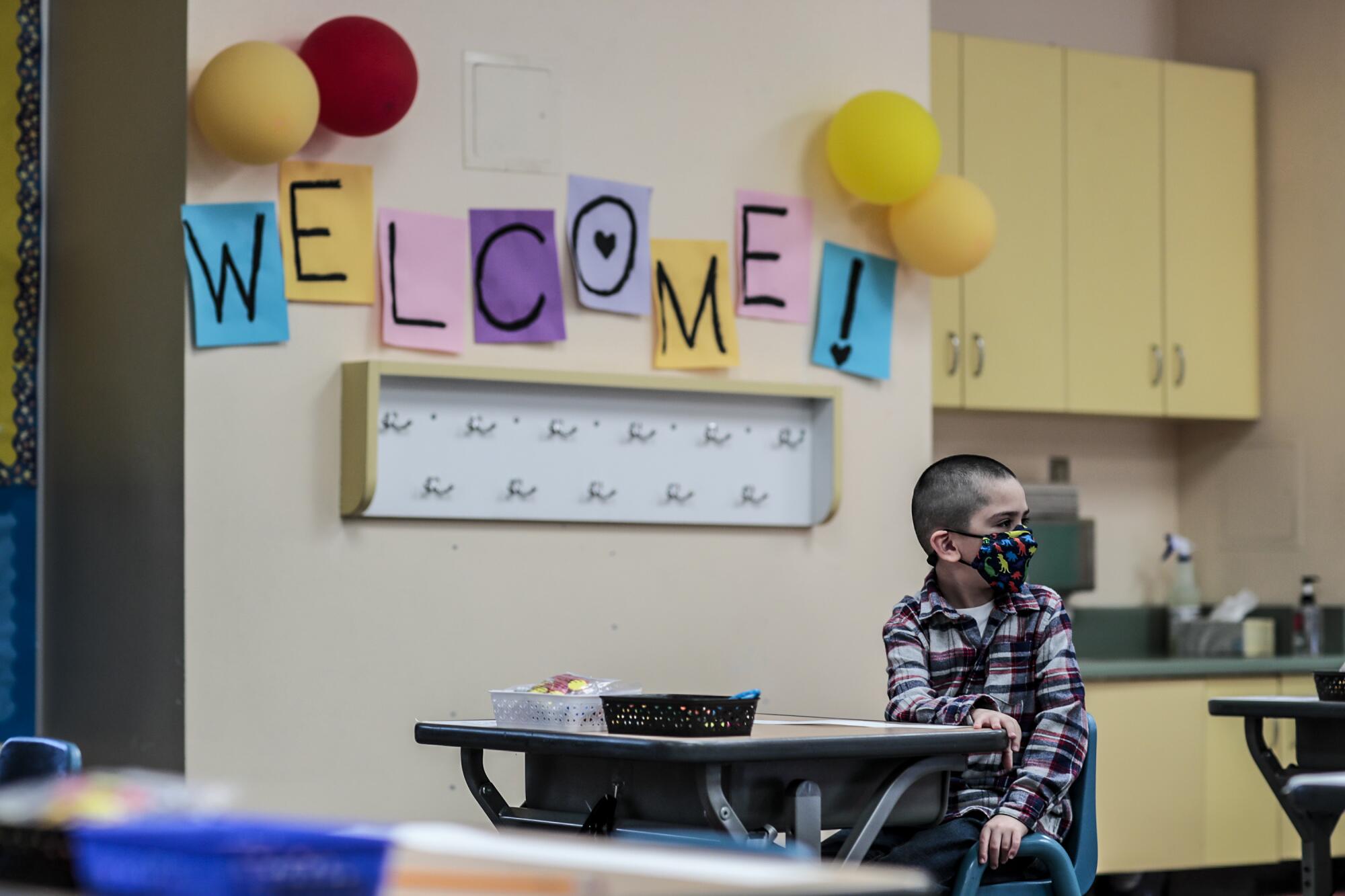 A child sits in front of a sign on the wall that says "Welcome!"