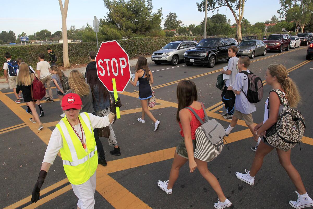 A crosswalk attendant stops traffic along Eastbluff Drive as students make their way to Corona del Mar High School in September.