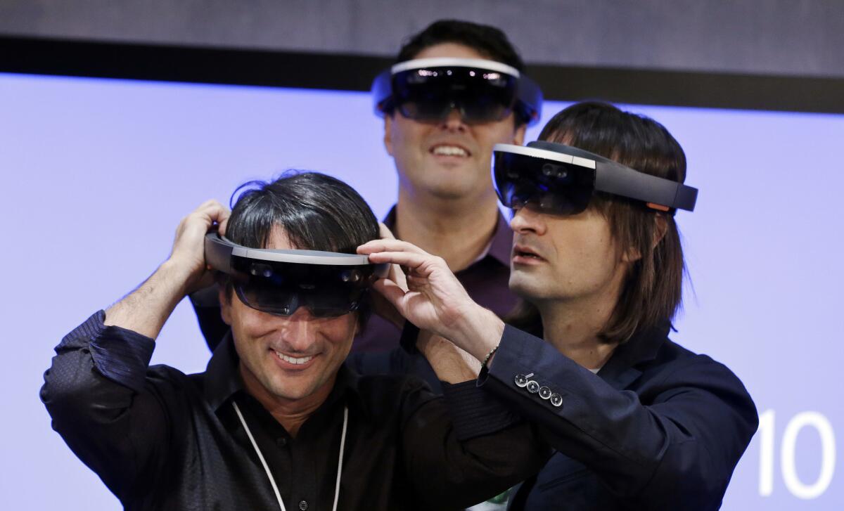 Microsoft's Joe Belfiore, left, smiles as he tries on a HoloLens device with colleagues Alex Kipman, right, and Terry Myerson following an event in Redmond, Wash., on Jan. 21.