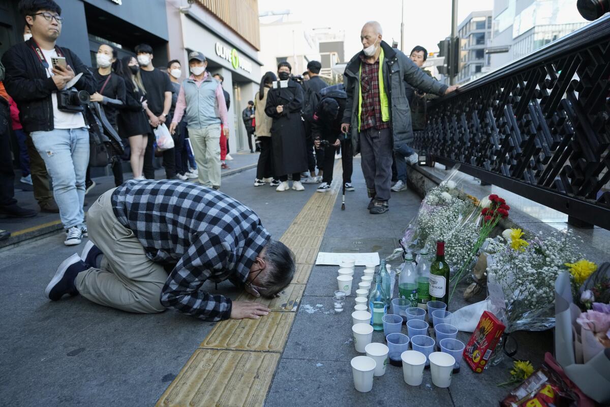 A man kneels and rests his head on the ground in front of a makeshift memorial.
