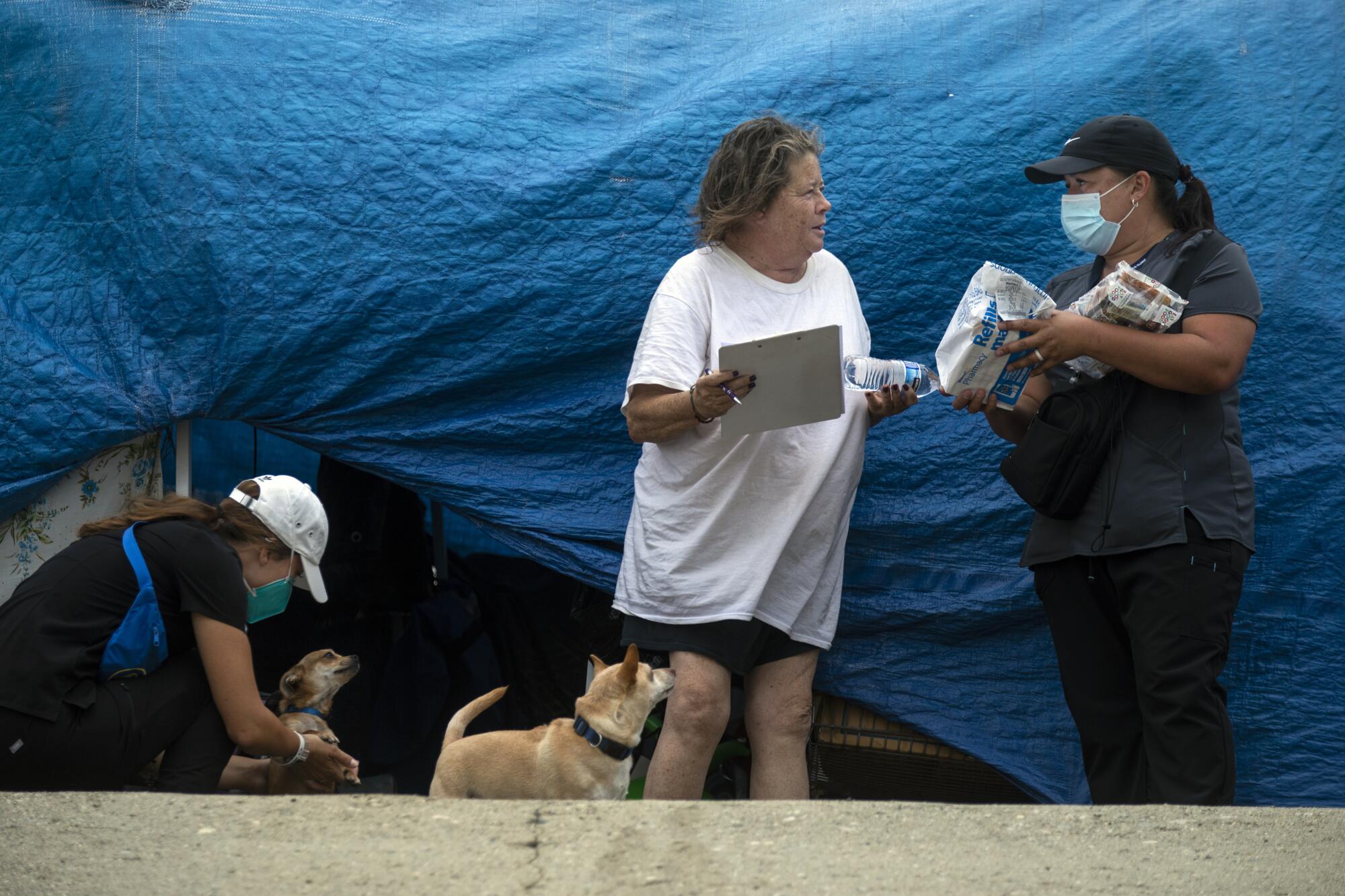 Members of the street medicine team talk to a homeless woman standing in front of blue tarps.