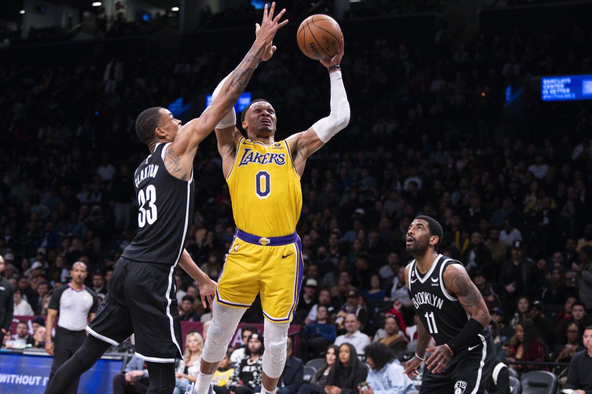 Lakers' Russell Westbrook looks to shoot a layup while defended by Brooklyn Nets' Nic Claxton and Kyrie Irving.