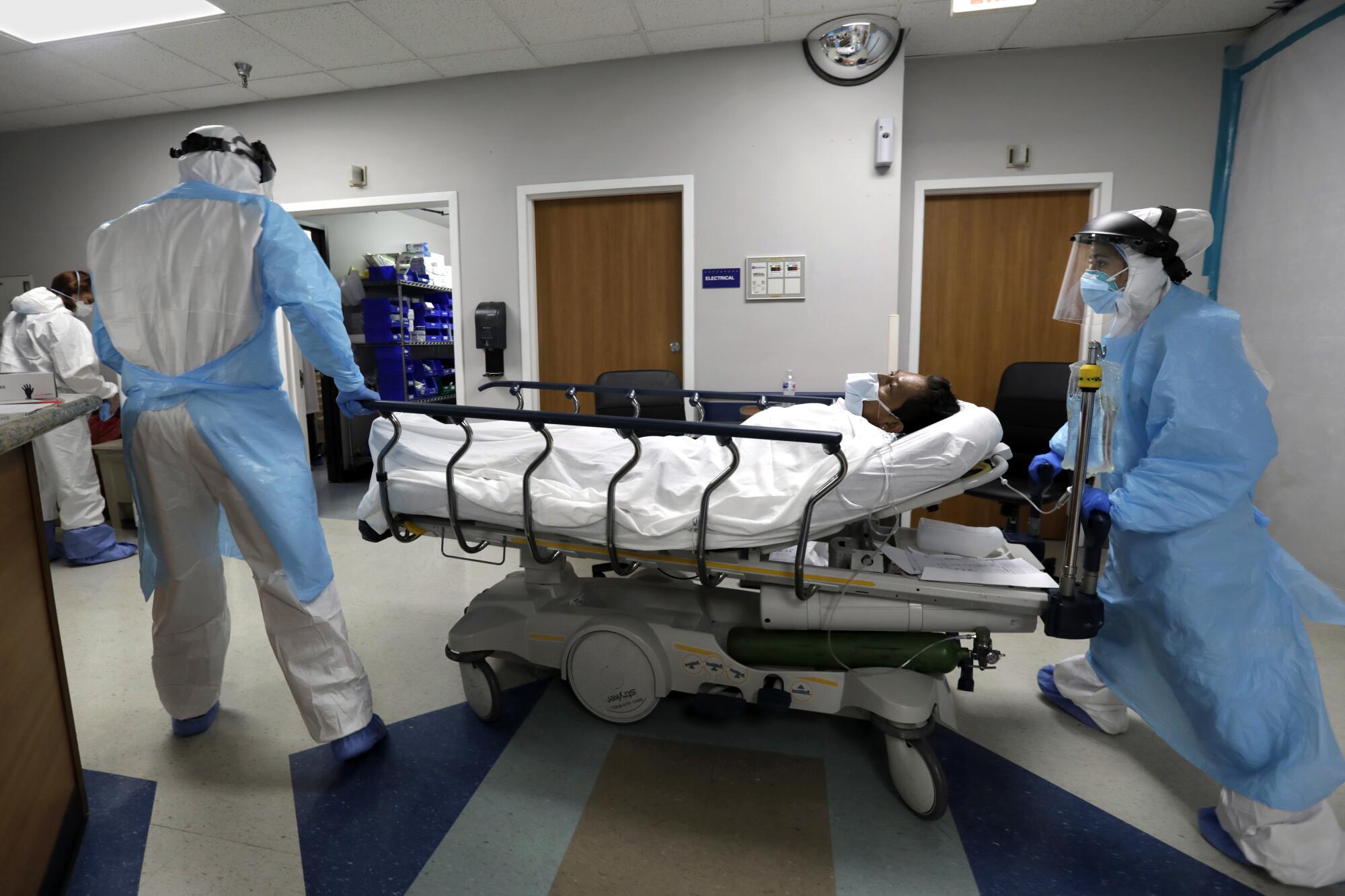 Anita Pandey, right, chief nursing officer for the hospital's COVID unit, wheels newly arrived patient Eliazar Angel Rodriguez from the ER with Alan Araiza, left, the medical student volunteer running the unit.