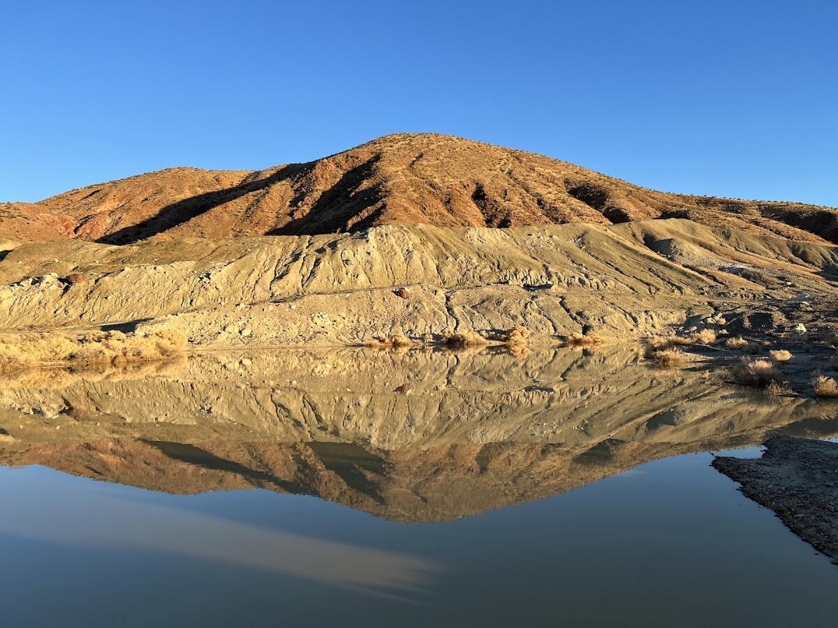 A hill above a pool of water is reflected on the water's surface