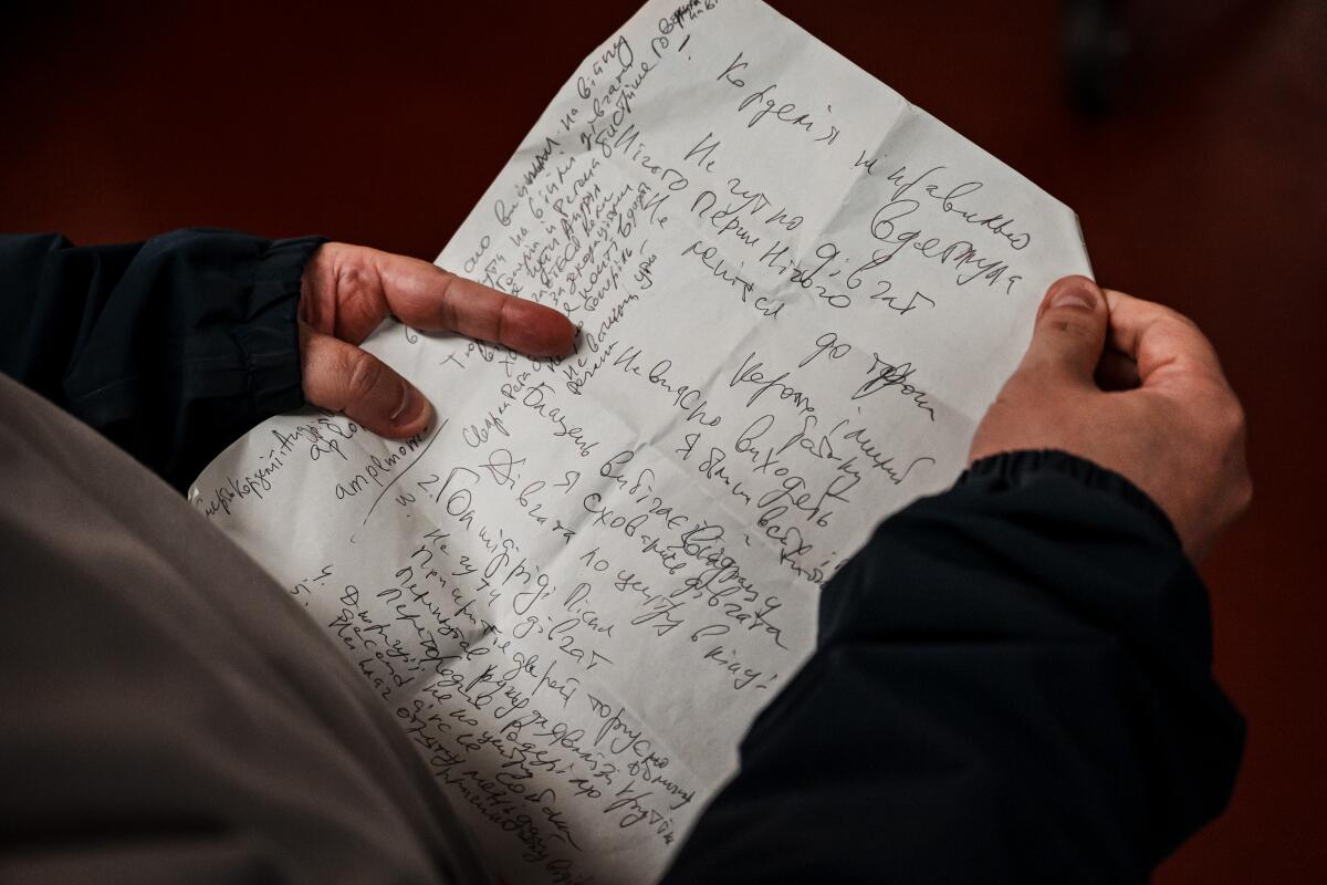 A man's hands hold a page of handwritten notes. 